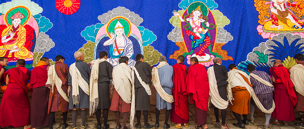 Group of monks and lay people rolling large tapestry Thangka in Bhutan